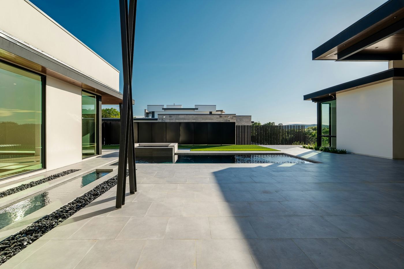 A modern home's pool terrace in hard midday sun, with long shadows across pale stone