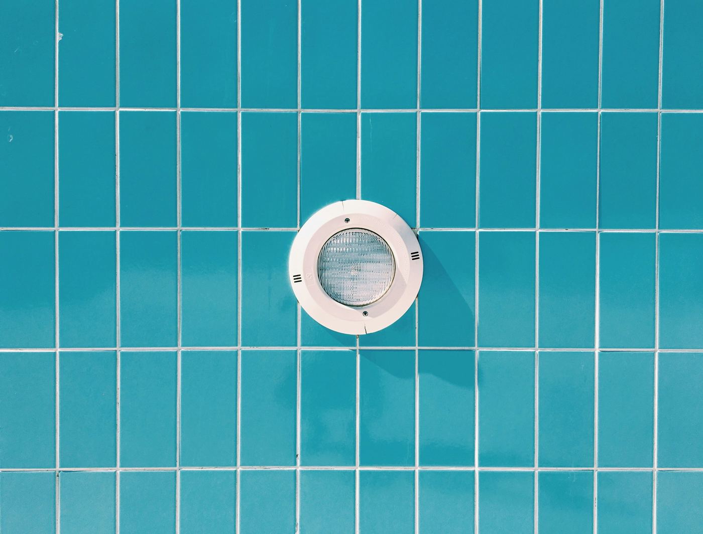 A round underwater pool light set into blue tile