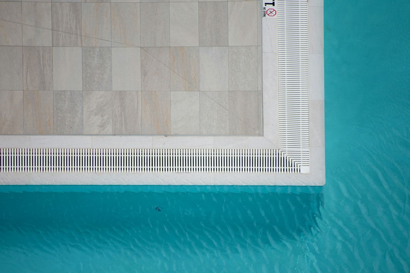 Overhead view of a pool's stone edge and gutter grate meeting the water